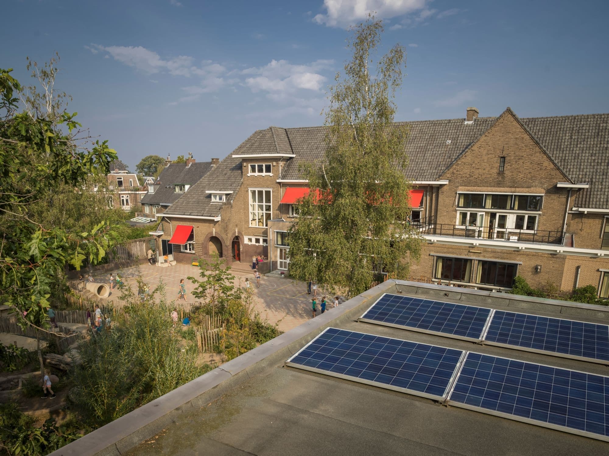 zonnenpanelen op een dak met op de achtergrond een oud schoolgebouw